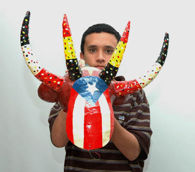 Anthony Paul Martinez holding four horned mask; Apprenticeship - Puerto Rican carnival mask making; 2007: Holyoke, Massachusetts; Painted papier mâché